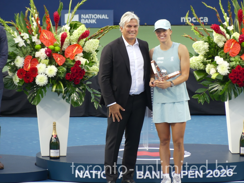 Iga Swiatek is holding her Trophy and posing with Karl Hale, 