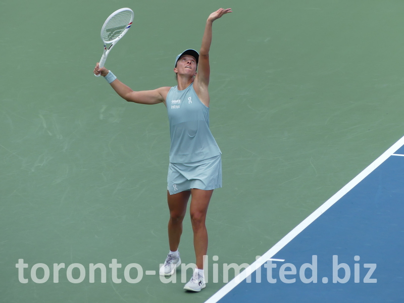 Iga Swiatek is in the serving posture with a high-toss ball. 