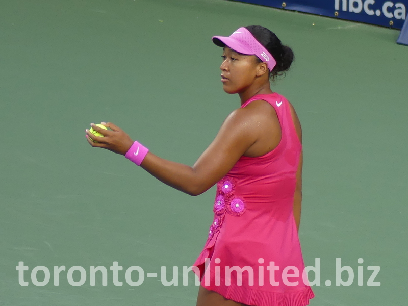 Naomi Osaka, with well-manicured hands, holds the tennis ball ready to serve.
