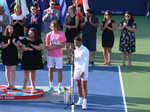 Rafael Nadal in front of microphone, his Trophy and Stefanos Tsitsipas on the left, also holding his Trophy.